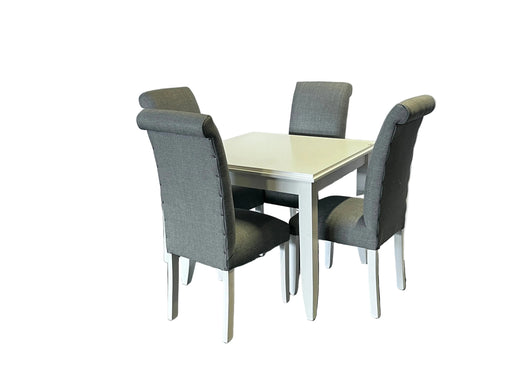 Dining table set with four gray chairs against a white draped backdrop