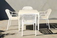 White outdoor table with four matching chairs on a concrete patio.