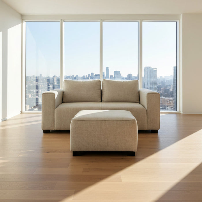 Beige sofa and ottoman in a room with large windows overlooking a cityscape.