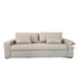 A light beige upholstered sofa with matching throw pillows, photographed in a showroom setting with a white protective drape and dark gray floor visible.