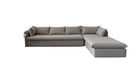 A light gray sectional sofa with a chaise lounge is shown in a showroom, partially covered by a large white sheet held up by people on both sides. A brown patterned rug lies in front of the sofa.