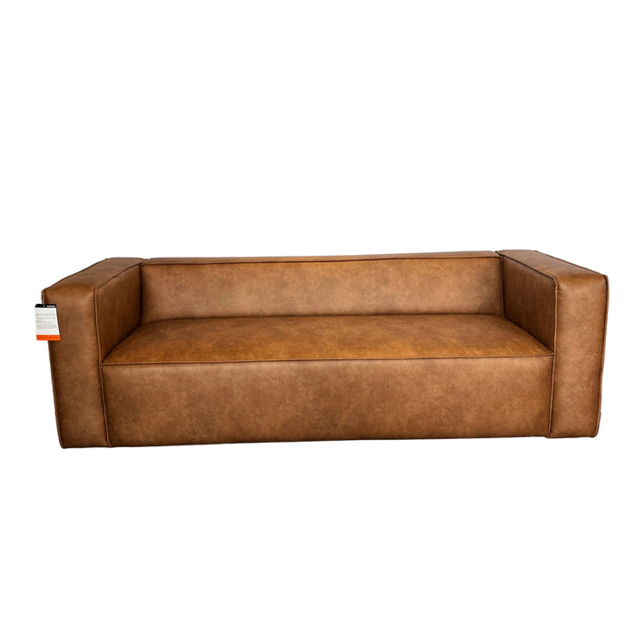 A brown upholstered bench or low sofa shown indoors on a white drape, with a carpeted floor and store-like surroundings visible.