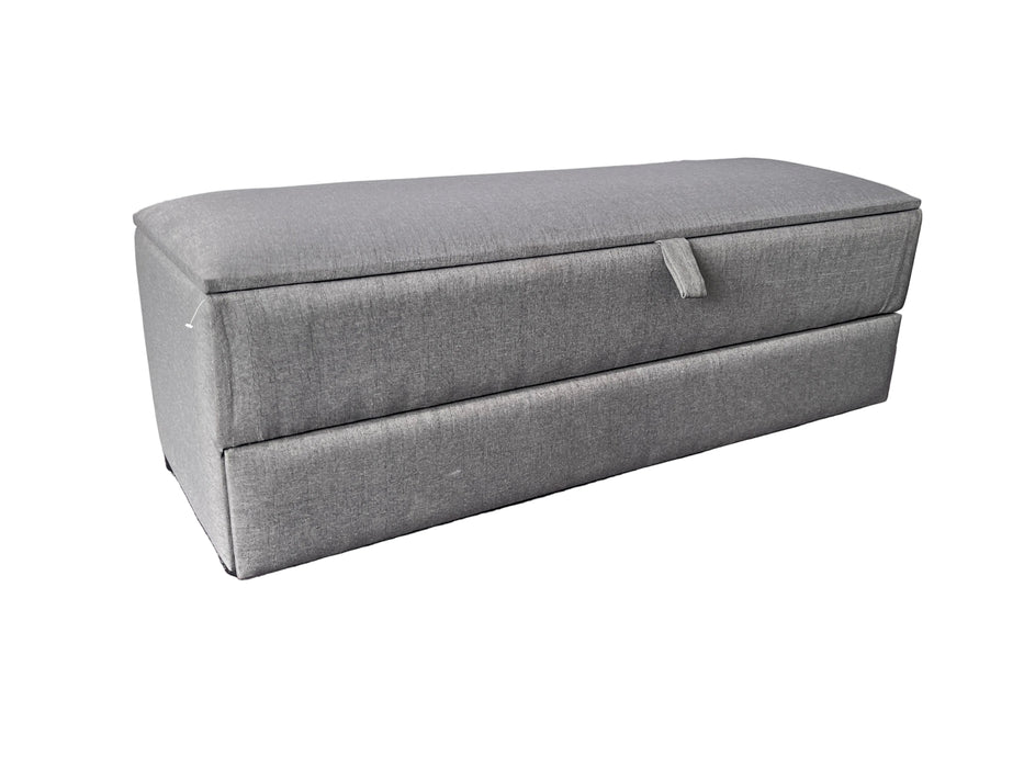 Gray storage ottoman on a purple floor with a white draped background