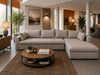 A large light beige sectional sofa with a chaise lounge in a modern, well-lit living room. The sofa is styled with matching throw pillows and is positioned on a brown patterned area rug with a round wooden coffee table in front of it.