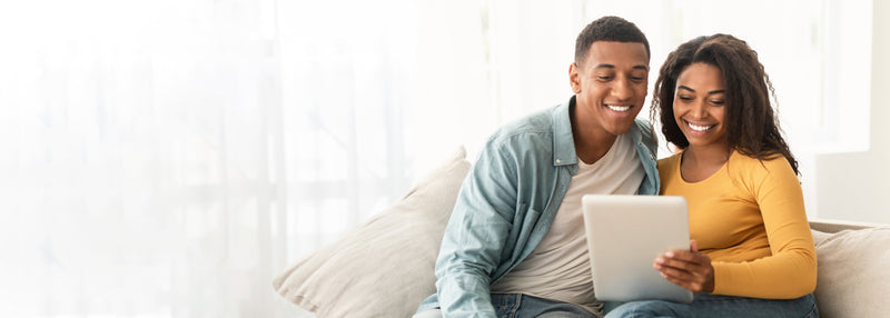 Couple sitting on a couch together, using a tablet.
